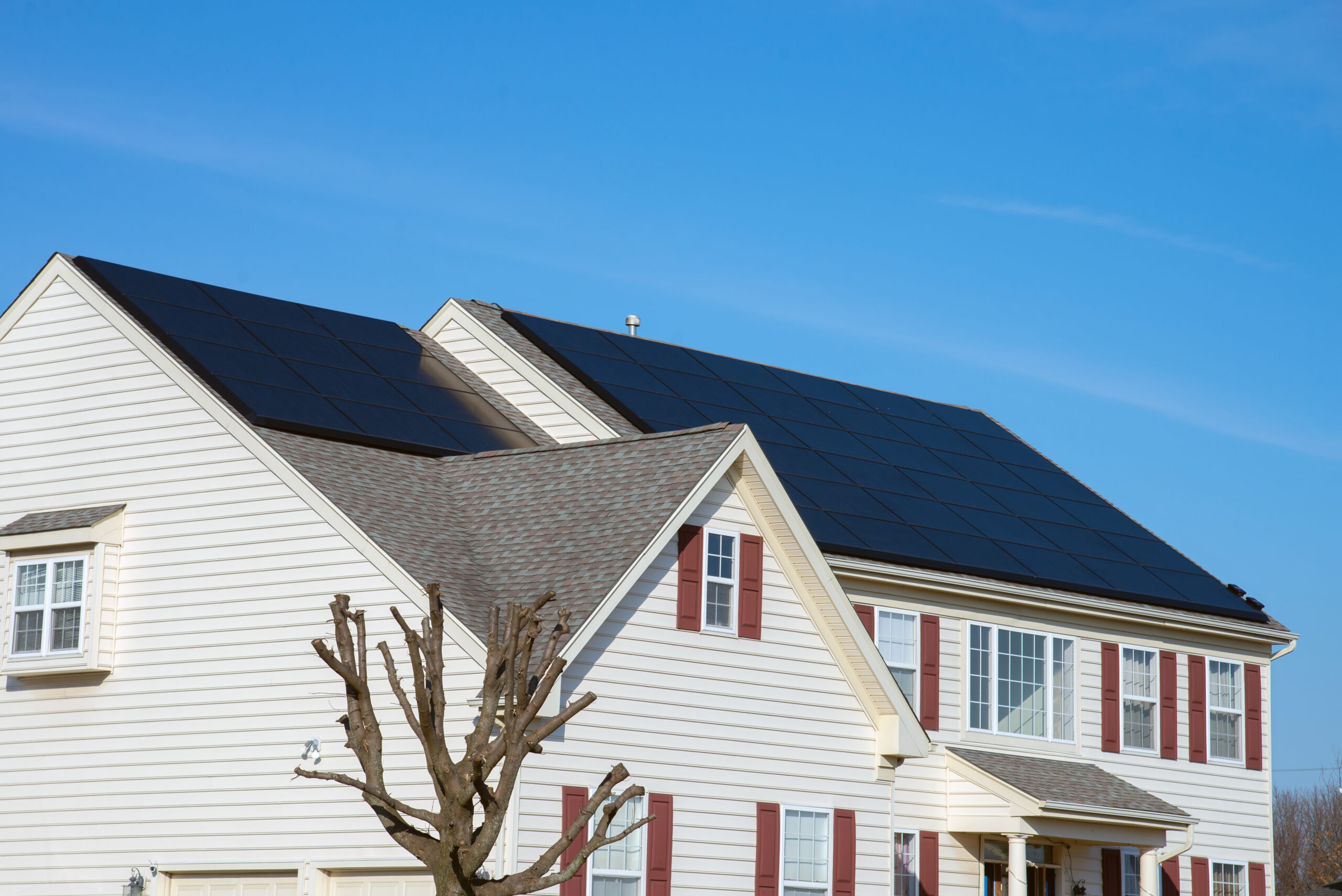 Two-story white house with red shutters and solar panels on an asphalt shingle roof