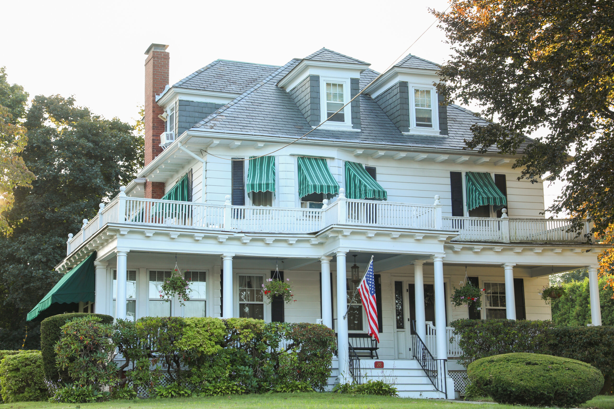 Three-story white house with an asphalt shingle roof, a balcony, and a porch