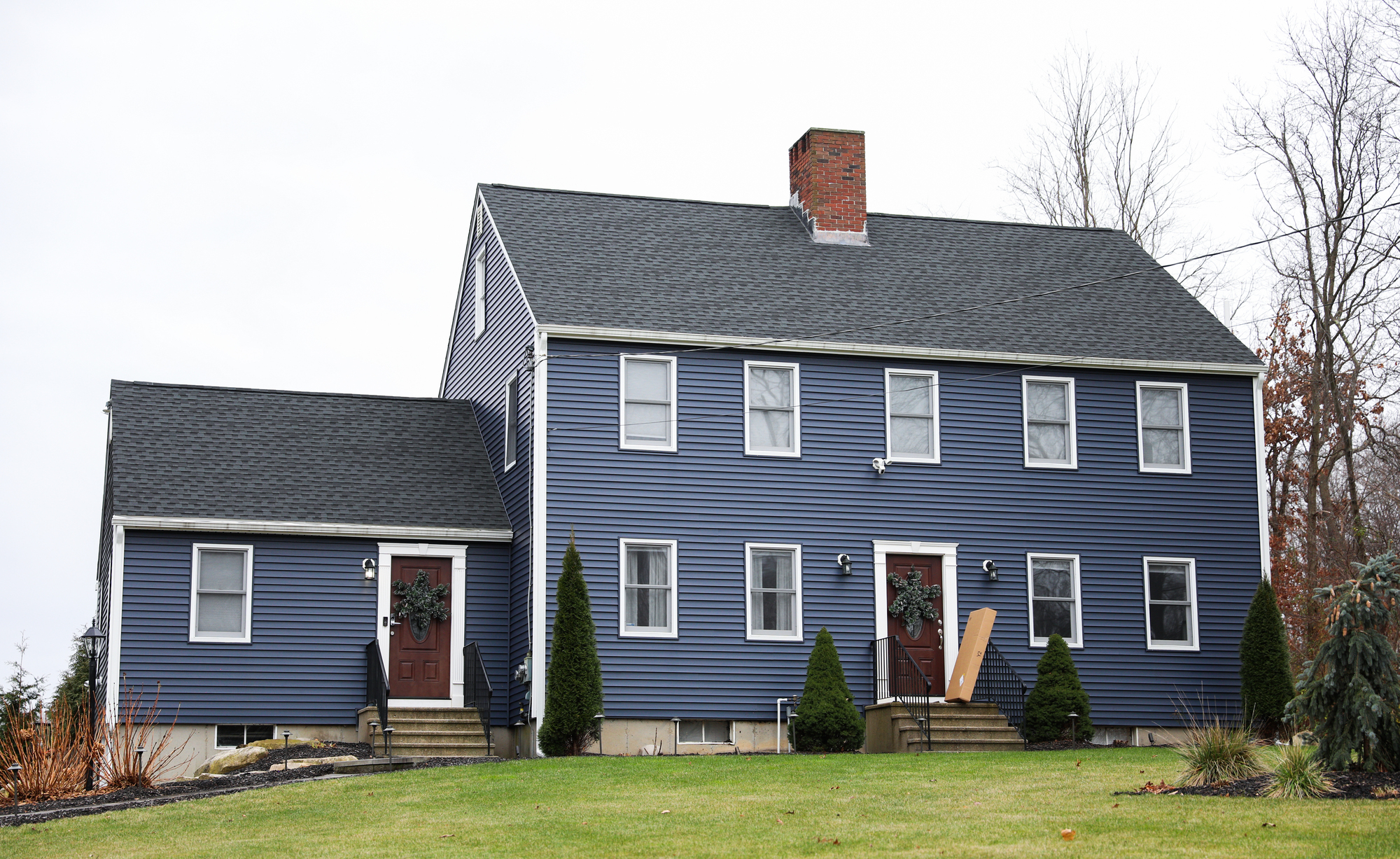 A large house with dark blue siding on a hill with green grass.