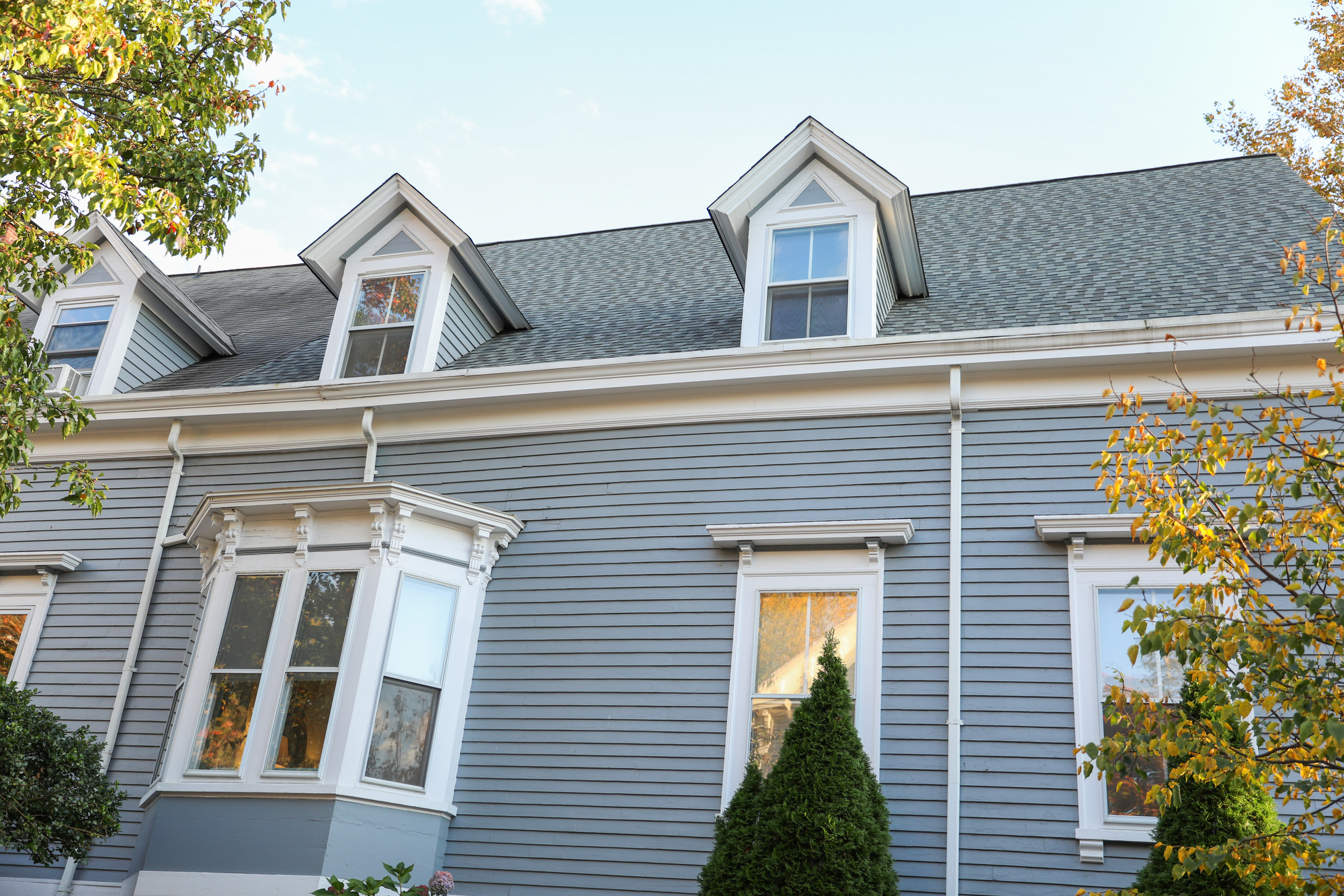 Gray siding on the side of a two-story house with a shingle roof