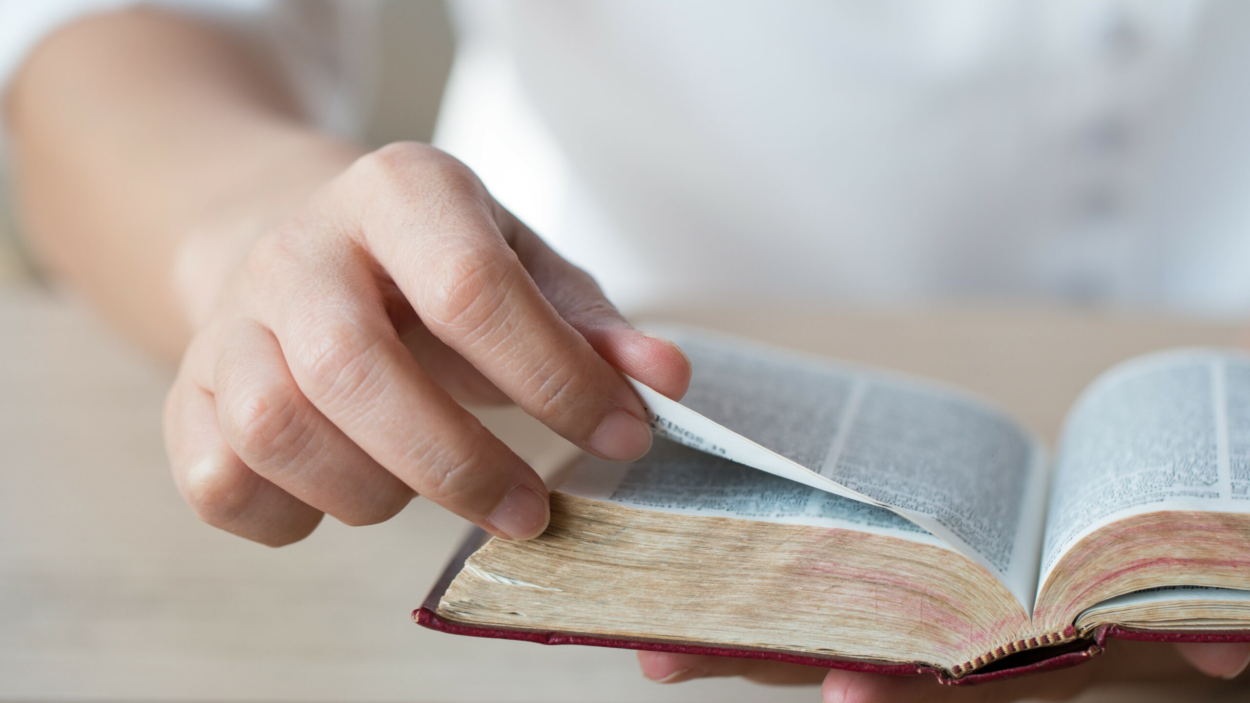 A close-up of a man’s hands holding a bible and turning a page