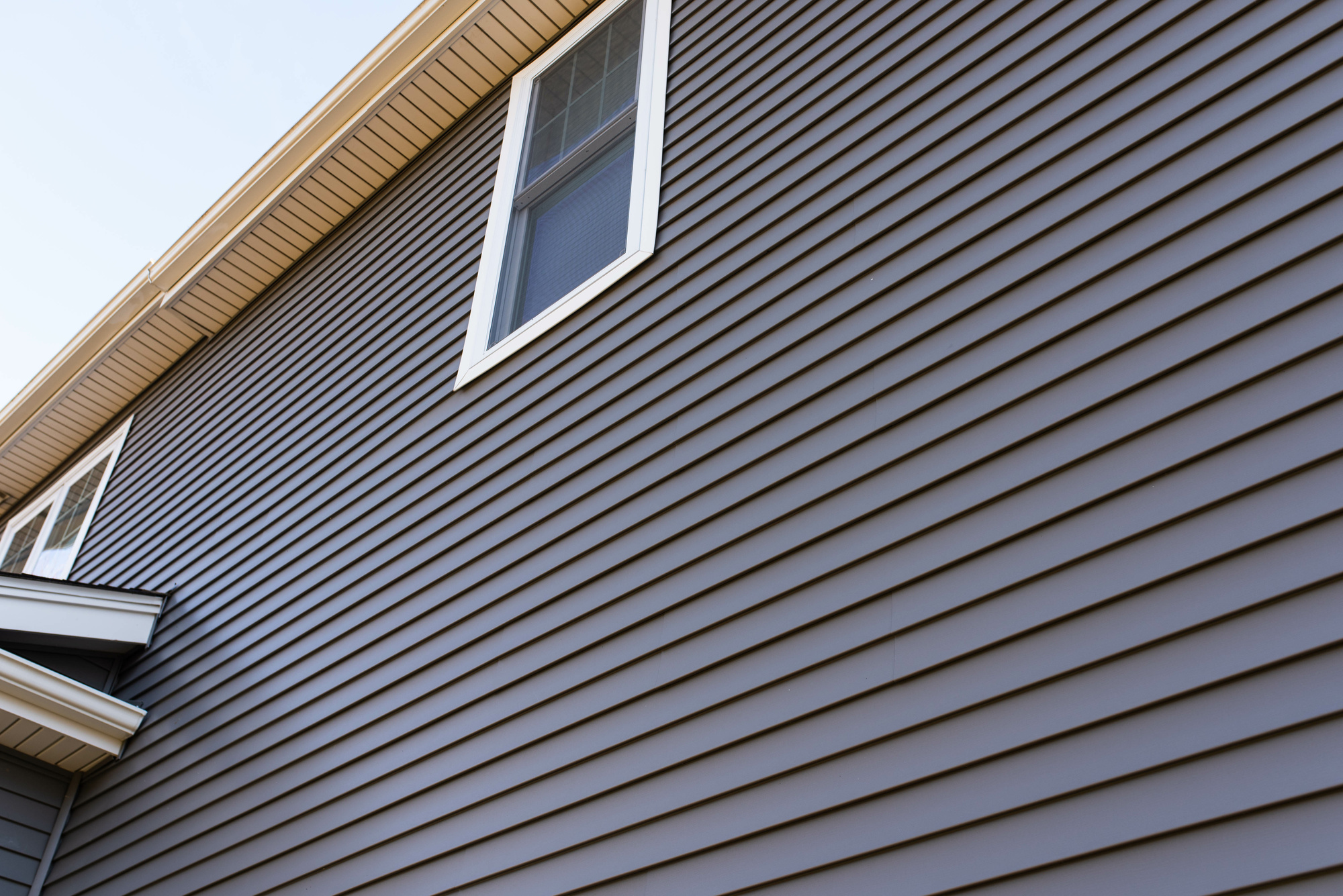 Looking up at a two-story house with gray siding and a white window
