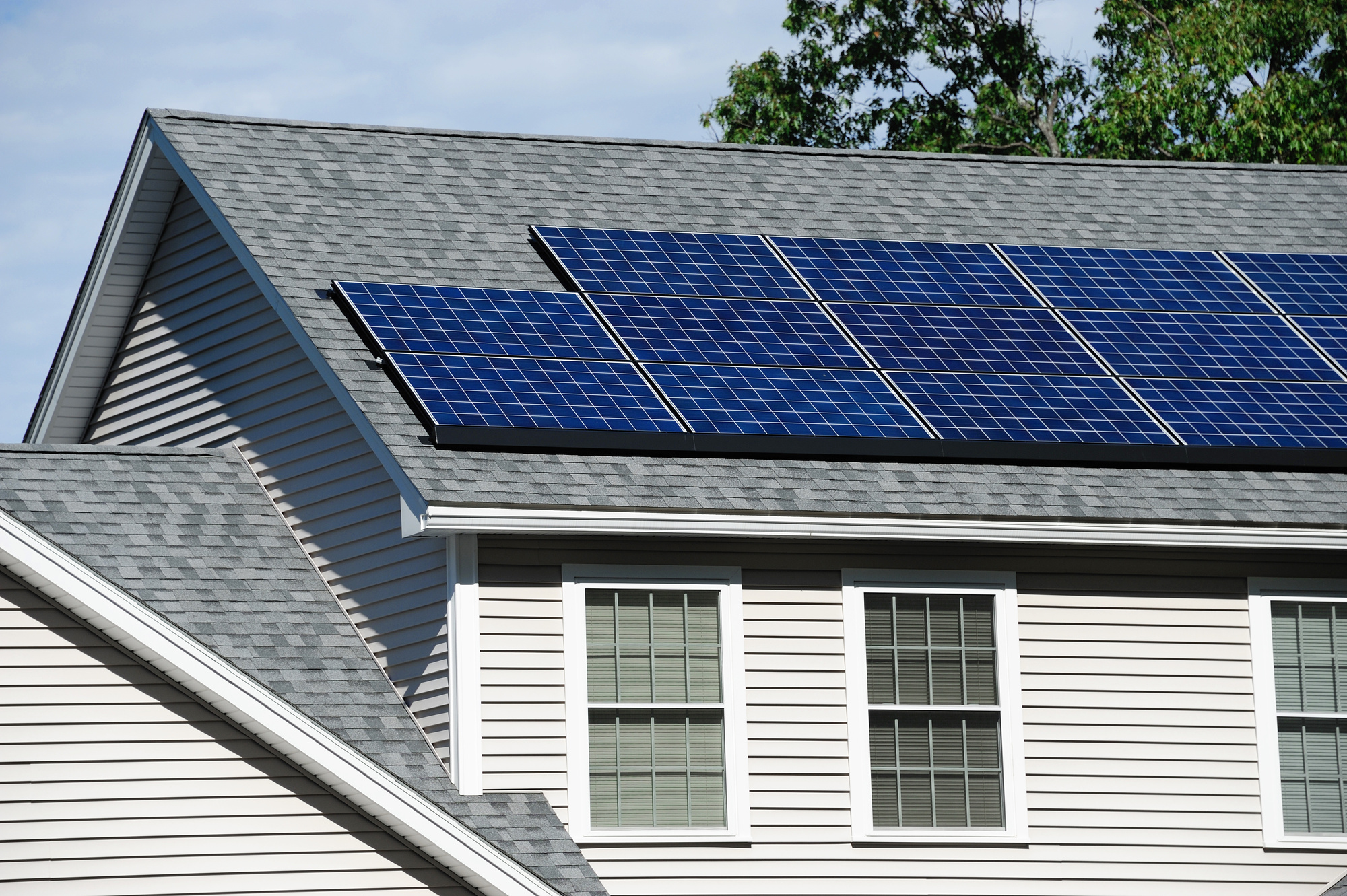 Closeup of solar panels on an asphalt shingle roof on a light gray house