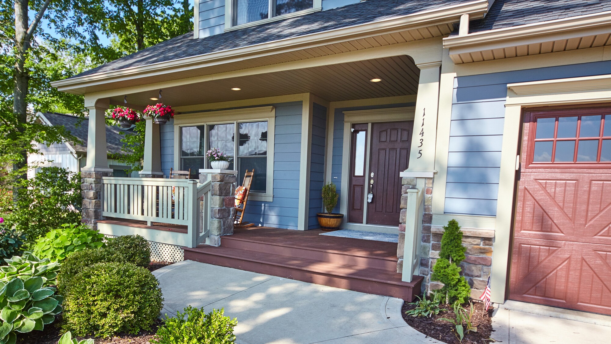 Modest house with white siding in Southwestern Ohio with a white fence and a landscaped front yard. A bush with red flowers is in the foreground, just beyond the gate.