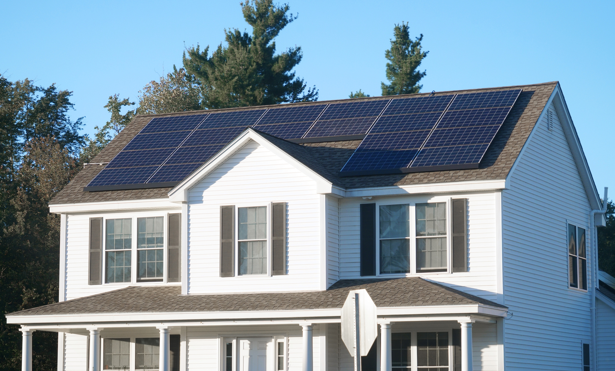 Solar panels on the shingle roof of a two-story white house